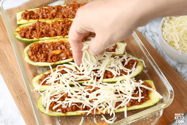 sprinkling cheese on ground beef stuffed zucchini boats