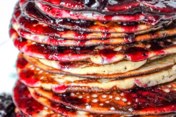 tall stack of almond flour pancakes topped with juicy blueberries and syrup