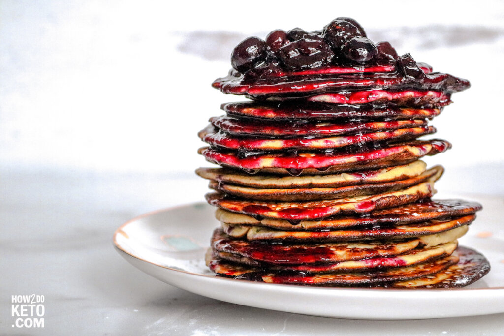 stack of thin, almond flour pancakes topped with juicy blueberries and syrup