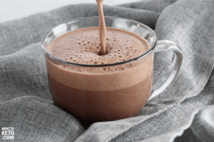 pouring keto hot chocolate into a clear glass mug