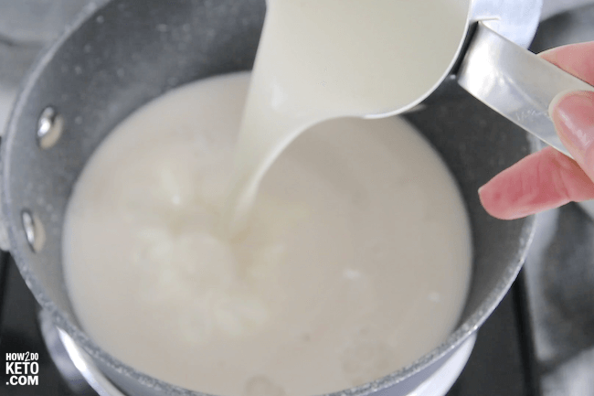 pouring heavy cream into a saucepan of milk