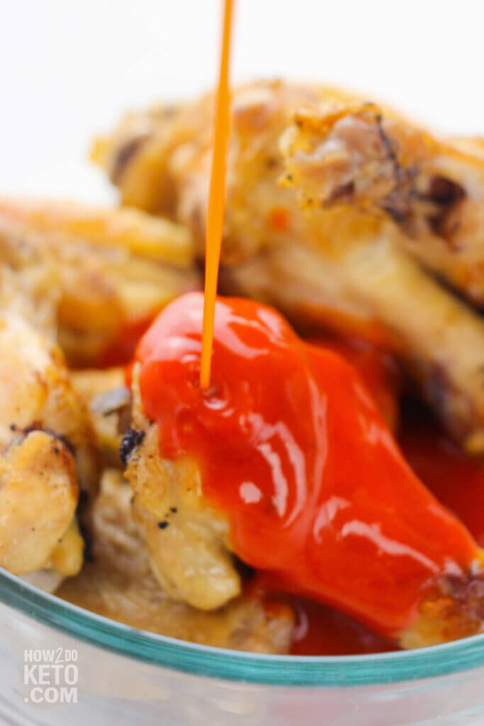 pouring buffalo sauce on chicken wings in bowl