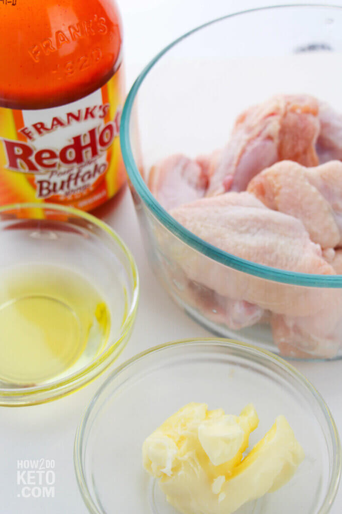 raw chicken wings in bowl with buffalo sauce bottle