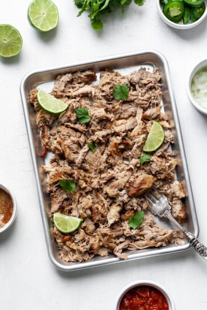 carnitas in sheet pan with lime wedges